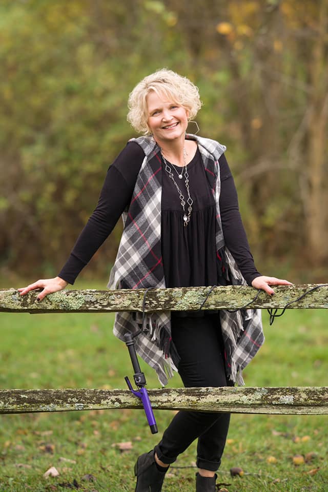 Woman posing by a wooden fence.